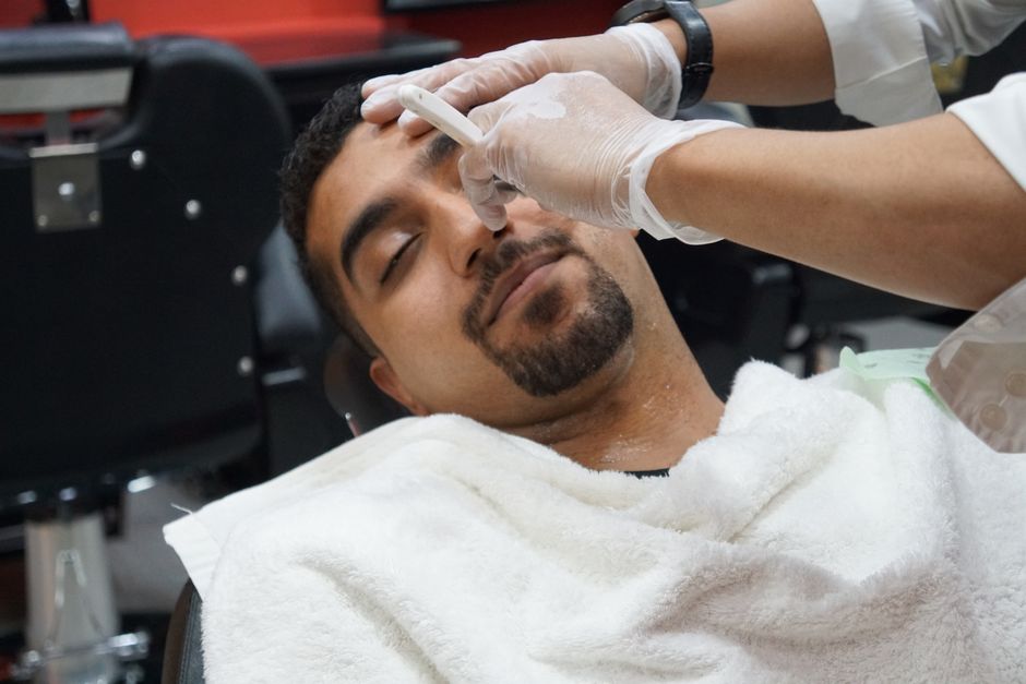 Barber při klasickém holení žiletkou, detailní záběr